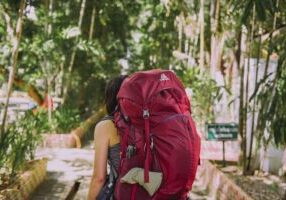 Woman carrying a heavy backpack representing the cost of wearing your armour and carrying protective patterns through life.